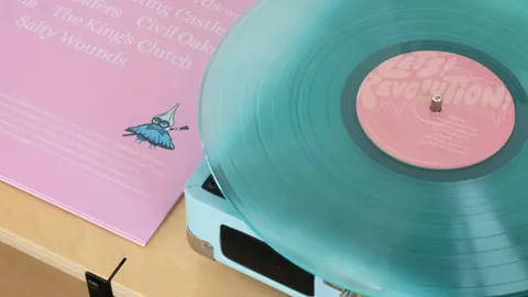 The translucent teal record playing on a pale blue portable turntable, the back of the sleeve and its track list propped behind it